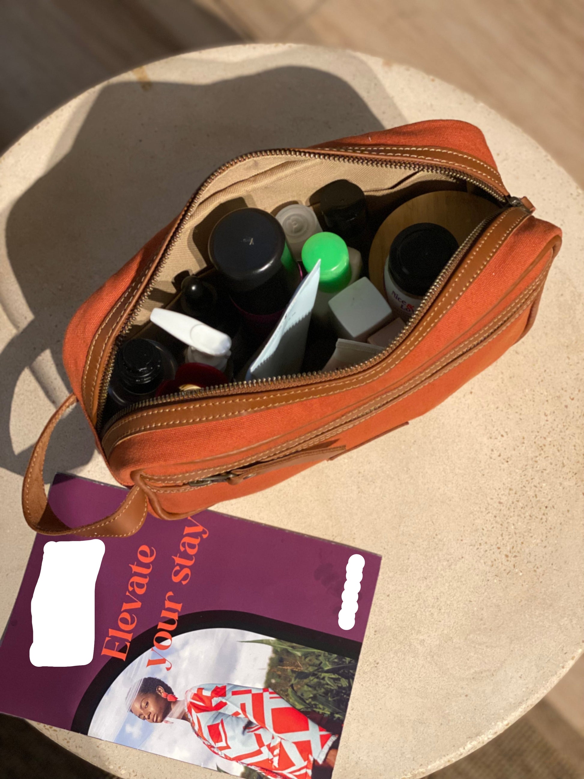 Open canvas and leather travel pouch/washbag with toiletries on a beige surface,