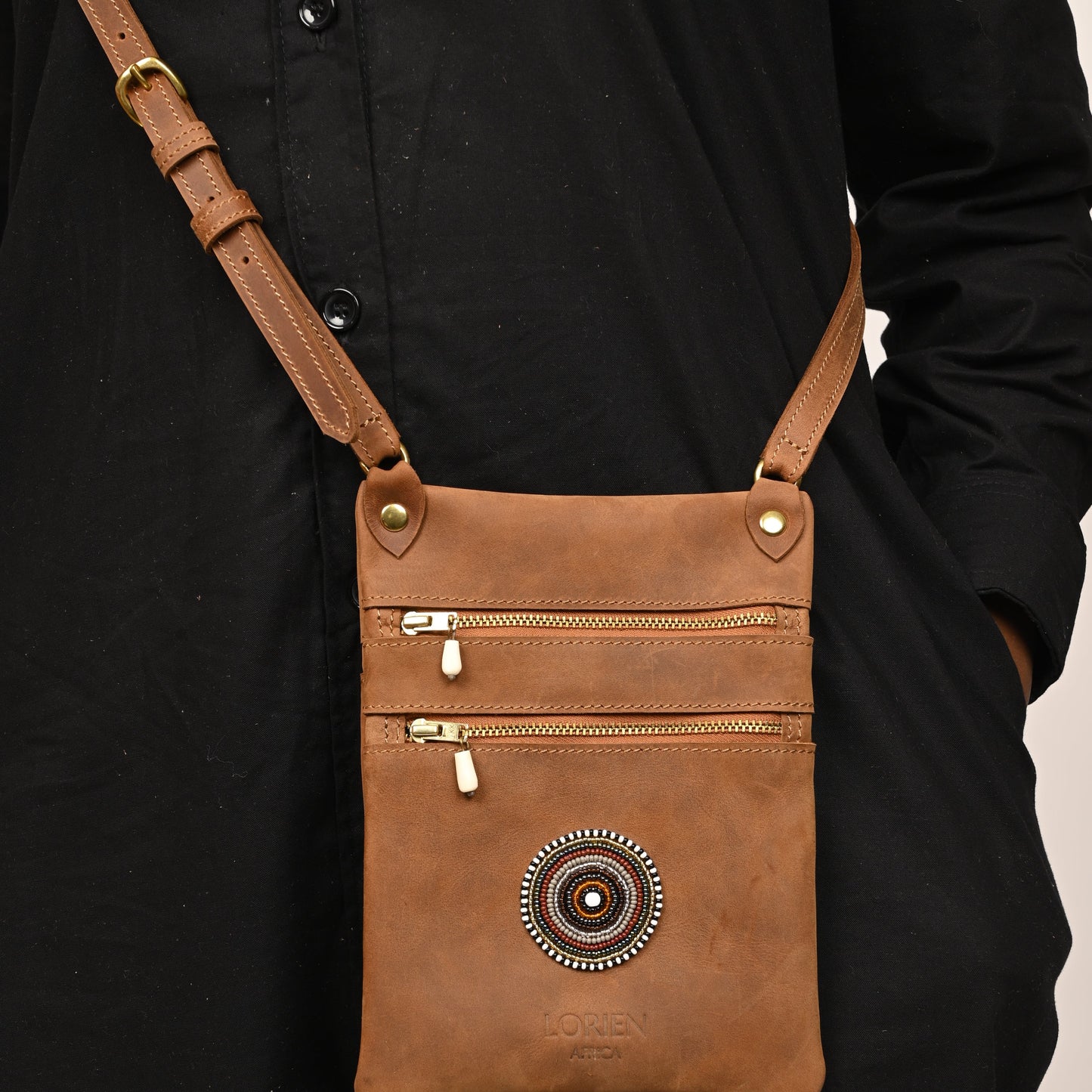 Brown leather crossbody bag with decorative emblem on a black background