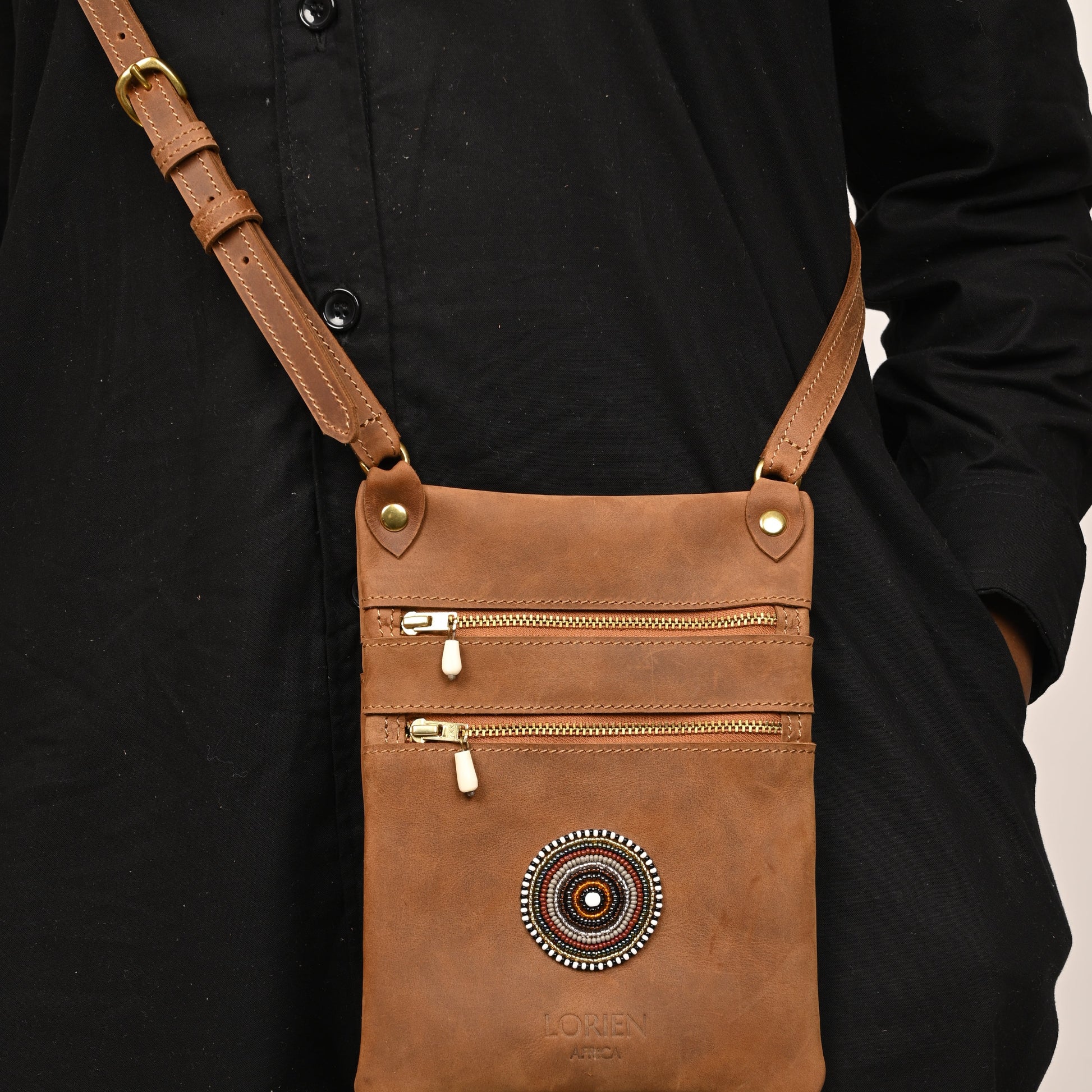 Brown leather crossbody bag with decorative emblem on a black background