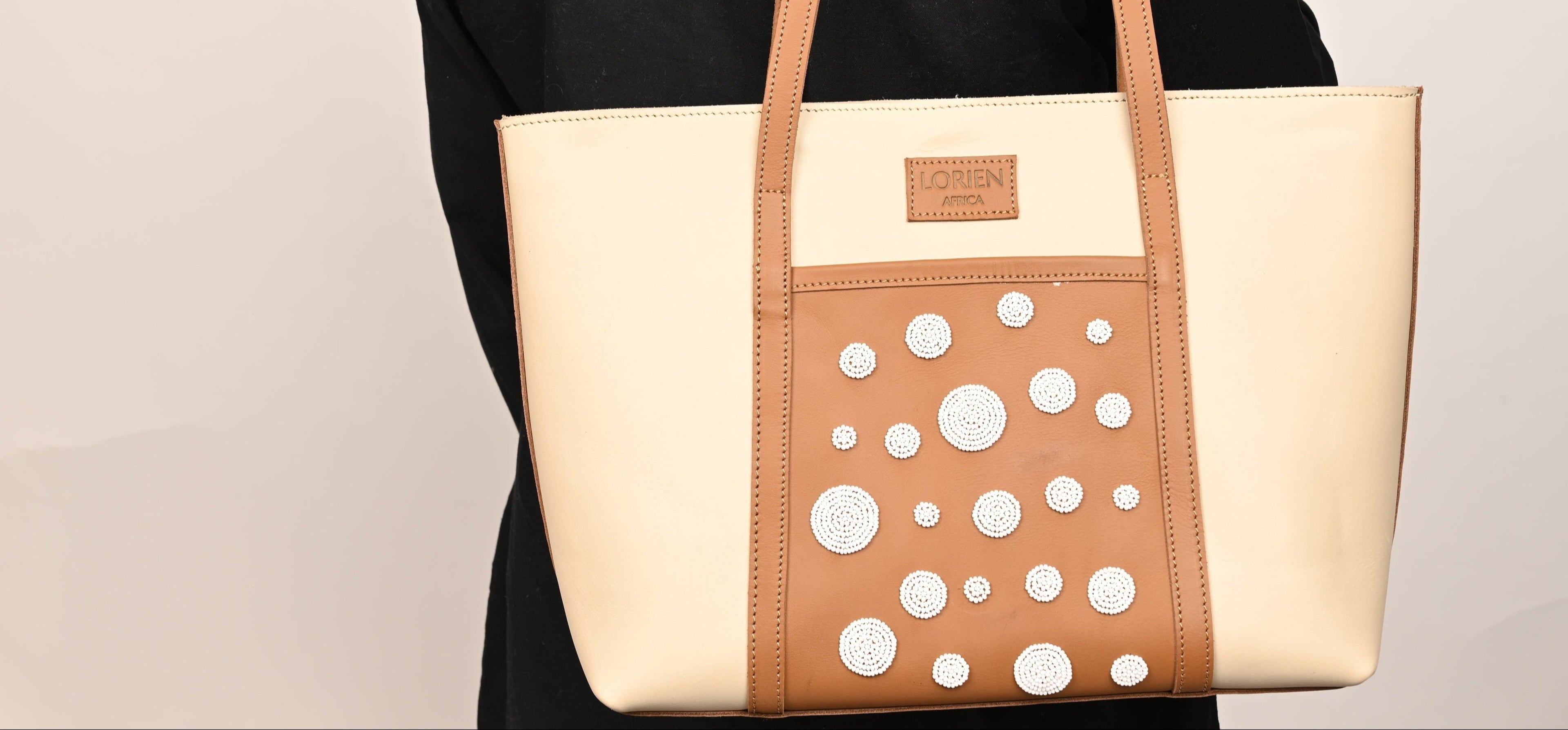 Beige tote bag with white polka dots held by a person wearing a black outfit on a beige background